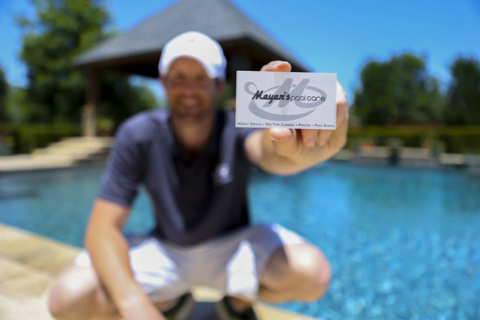 A Meyer's Pool Care team member holding the company card beside a clean pool